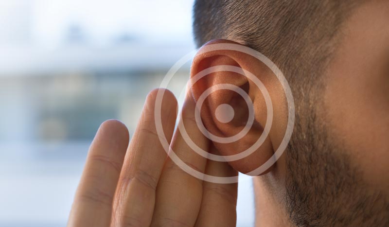 Seitenansicht eines Mannes, der die Hand hinter das Ohr legt, überlagert mit einer grafischen Darstellung von Schallwellen, Stichwort Hörgesundheit.
(c) AdobeStock