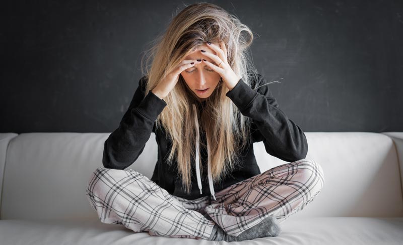 Die ultimative Migräne-Checkliste: Ihr Wegweiser aus dem Schmerzlabyrinth 1 Eine junge Frau mit blonden Haaren sitzt mit überkreuzten Beinen auf einem weißen Sofa und hält sich die Hände an den Kopf. Sie hat Schmerzen, Schläfenmassage, dunkler Hintergrund. Fokus: Migräne-Schmerz und Leiden.
(c) AdobeStock