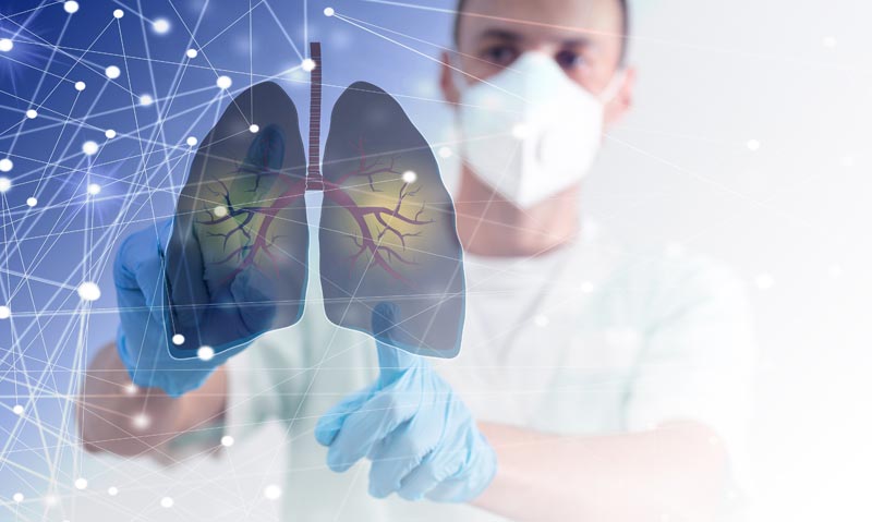 Ein Arzt mit Atemschutzmaske und Handschuhen zeigt auf eine virtuelle, leuchtende Darstellung der menschlichen Lunge in einem digitalen Netzwerk, Stichwort Pneumokokken-Impfung.
(c) AdobeStock