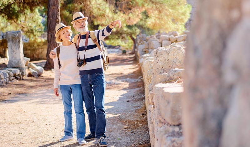 Älteres, fit wirkendes Paar mit Hüten steht Arm in Arm auf einem Ausgrabungsgelände, der Mann zeigt nach rechts oben, Stichwort Silver Nomad.
(c) AdobeStock