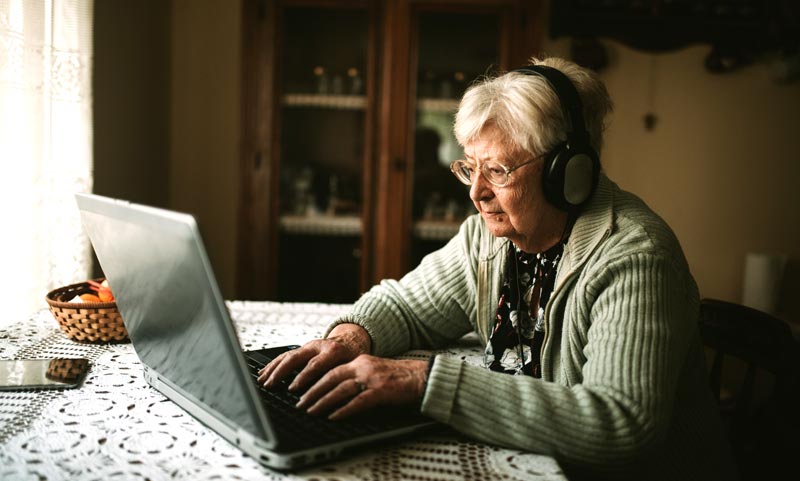 Ältere Frau nutzt konzentriert einen Laptop mit Kopfhörern und beweist kognitive Souveränität und digitale Autonomie im Alter, Stichwort Altersdiskriminierung.
(c) AdobeStock