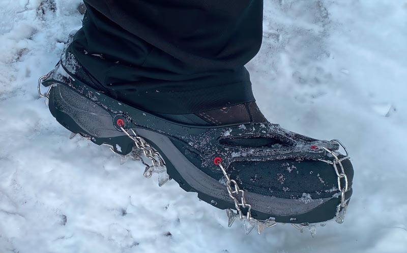 Nahaufnahme eines schwarzen Bergschuhs, an dem Spikes-Ketten (Grödel) befestigt sind. Der Schuh steht auf einer verschneiten Fläche. Die Ketten und Zacken sind gut sichtbar, Stichwort Altschneefelder.
(c) AdobeStock