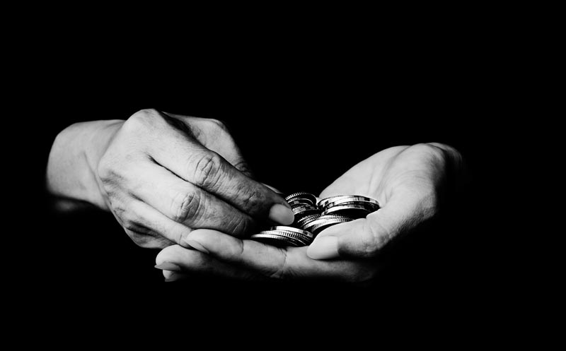 Schwarz-Weiß-Nahaufnahme von Händen, die mühsam Münzen in einer Handfläche zählen vor schwarzem Hintergrund.
(c) AdobeStock