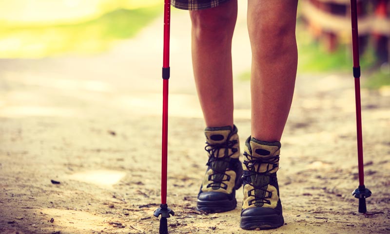 Adipositas-Therapie im Realitätscheck: Warum GLP-1 alleine uns nicht rettet 2 Nahaufnahme von den Beinen einer wandernden Person in robusten Wanderschuhen mit roten Trekkingstöcken auf einem unbefestigten Waldweg.
(c) AdobeStock