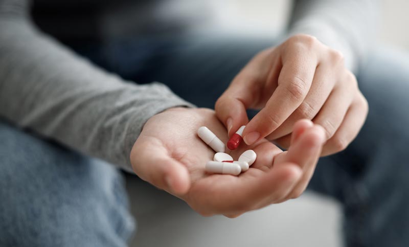 Körperliche Souveränität: Warum Fitness nicht aus der Apotheke kommt 1 Nahaufnahme der Hände einer sitzenden Person in Jeans, die eine Auswahl an weißen Tabletten und einer rot-weißen Kapsel in der offenen Handfläche hält.
(c) AdobeStock