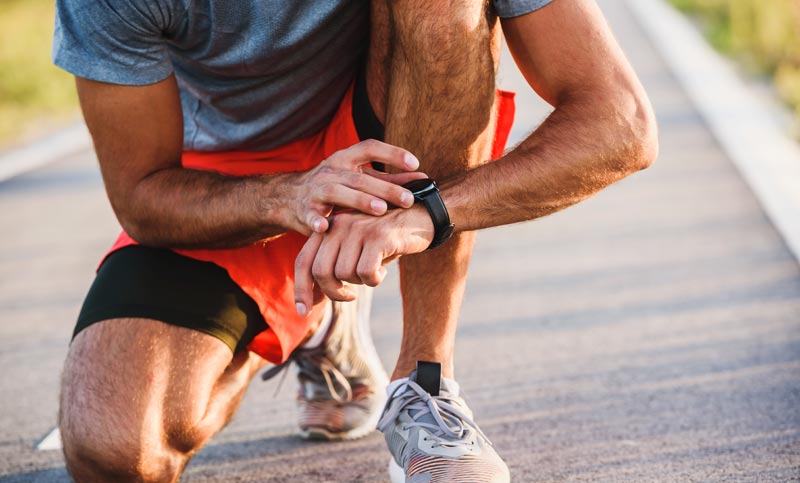 Ein sportlicher Mann kniet auf einer Straße und checkt seine schwarze Smartwatch am Handgelenk, um seine Herzfrequenz-Zonen und den VO2max-Wert während des Trainings zu überprüfen.
(c) AdobeStock