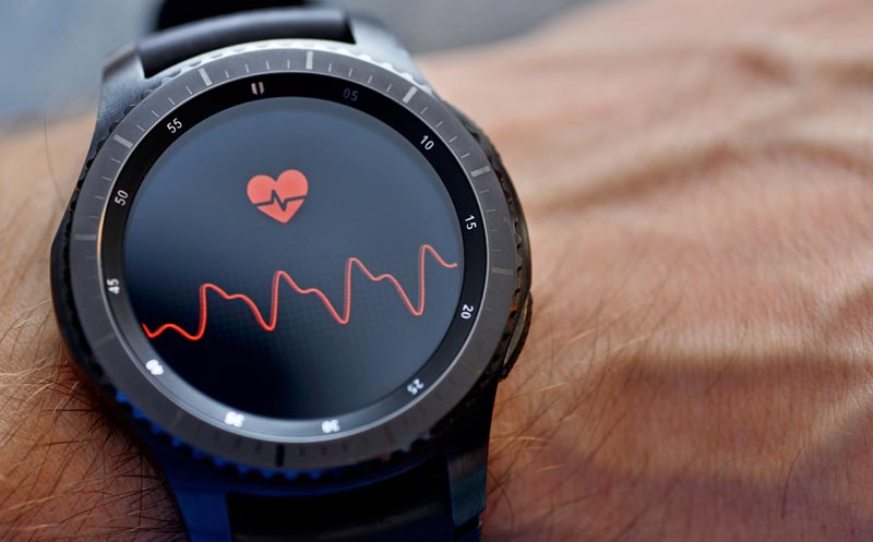 Wearables – Alter, Herzwerte und Fitness im Ü50-Check 1 Makroaufnahme einer schwarzen Smartwatch am behaarten Handgelenk eines Mannes, die ein rotes Herzsymbol und eine Pulskurve auf dem Display anzeigt, Stichwort Wearables – Alter.
(c) AdobeStock