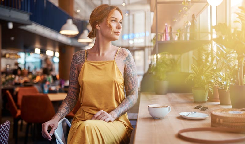 Radikale Selbsterkenntnis: Warum Sie alleine reisen im Alter als Ego-Stresstest nutzen sollten 2 Eine nachdenkliche Frau sitzt allein an einem Tisch im Café und blickt aus dem Fenster, um die eigene Gesellschaft stoisch auszuhalten statt durch alleine reisen im Alter abgelenkt zu werden.(c) AdobeStock