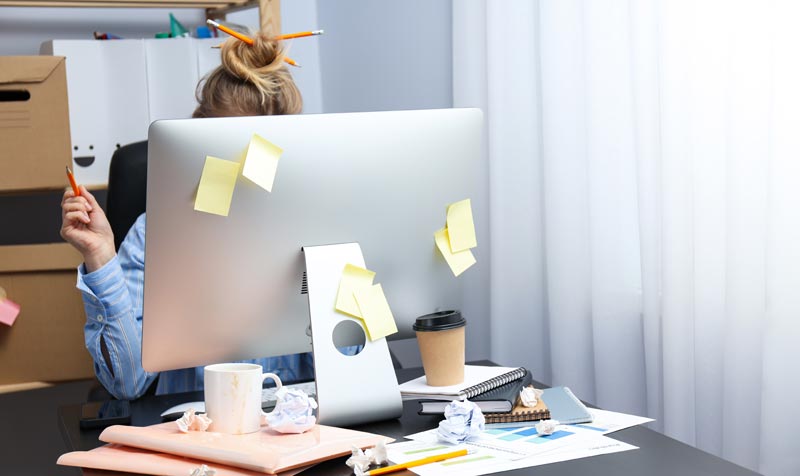 Digitaler Nachlass: Passwörter und Online-Konten richtig regeln 1 Rückansicht einer überforderten Person am Schreibtisch, deren Computerbildschirm chaotisch mit gelben Haftnotizen (Post-its) beklebt ist. Ringsherum liegen zerknülltes Papier und Kaffeetassen.(c) AdobeStock