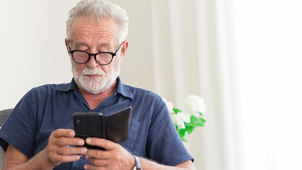 Gehirn fit halten im Alter: Smartphone schlägt Sudoku Ein älterer, konzentrierter Mann mit Brille nutzt fokussiert sein Smartphone, um sein Gehirn fit halten im Alter durch digitale Komplexität. (c) AdobeStock