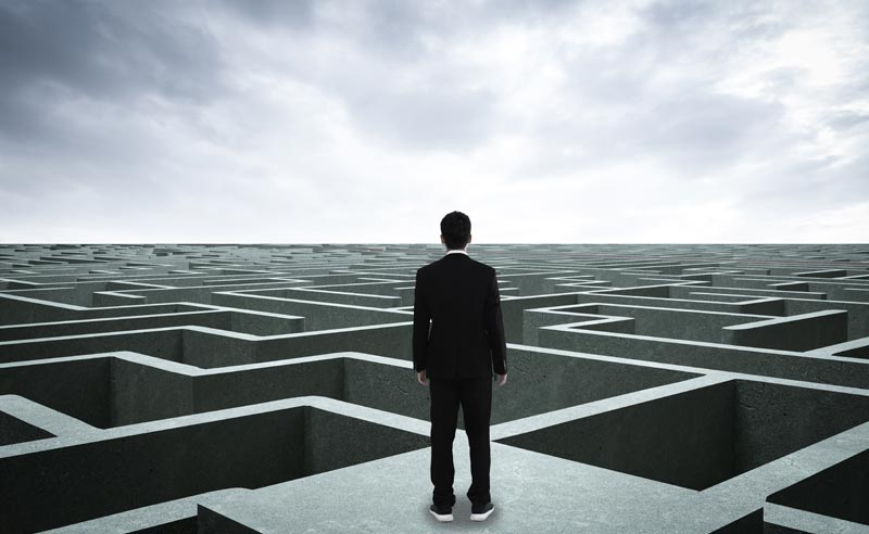 Unlearning: Warum Verlernen die härteste Disziplin im Alter ist 2 Eine stilisierte, monochrome Nahaufnahme eines Labyrinths aus Betonwänden mit klarem Licht- und Schattenspiel, davor steht ein Mann und blickt in die Weite des Labyrinths.(c) AdobeStock