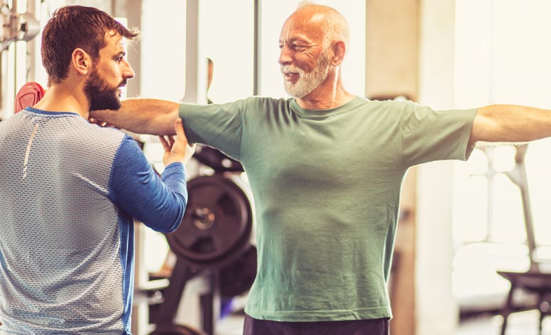 Abnehmspritze ab 50: Warum Fett schmilzt, aber die Substanz leidet 1 Älterer Mann absolviert Seitheben mit Hanteln unter Anleitung eines Trainers im Fitnessstudio.(c) AdobeStock