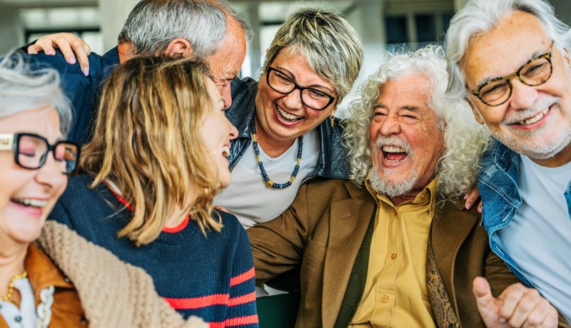"Wie bitte?!" – Warum Ignorieren bei der Hörgesundheit ein verdammt schlechter Plan ist 2 Eine Gruppe von Best Agern lacht ausgelassen und eng zusammenstehend bei einem geselligen Treffen.(c) AdobeStock
