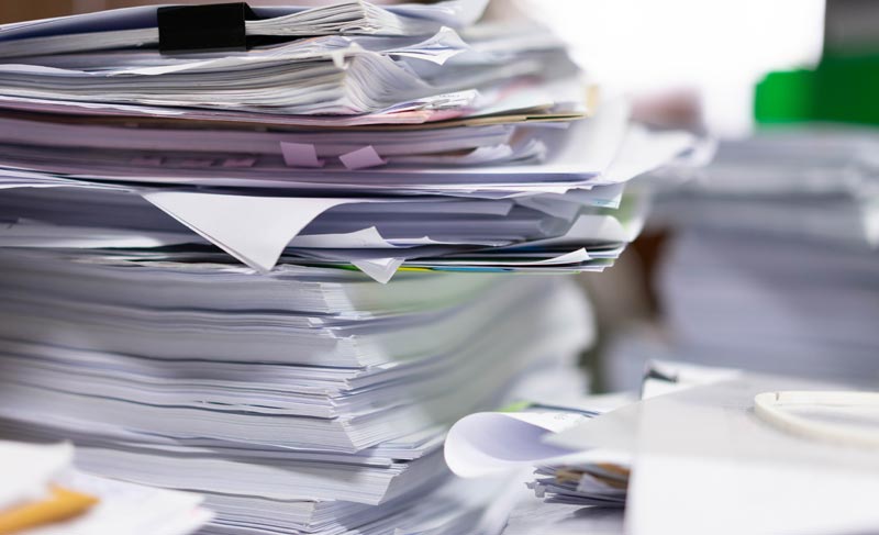 Migräne im Alter: Wenn moderne High-Tech-Medizin an der Kassenrealität scheitert 2 Ein riesiger, ungeordneter Stapel Papierdokumente und Akten im Büro.(c) AdobeStock