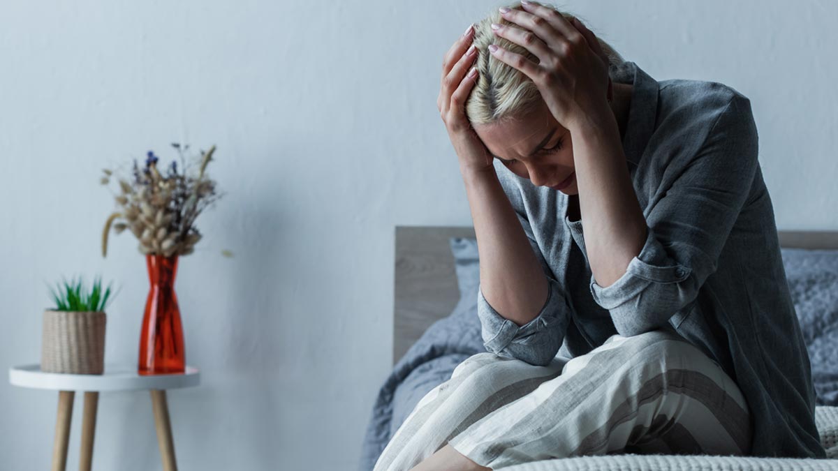 Migräne im Alter: Wenn moderne High-Tech-Medizin an der Kassenrealität scheitert Eine Person sitzt mit starken Kopfschmerzen und Migräne verzweifelt auf der Bettkante und hält sich den Kopf. (c) AdobeStock