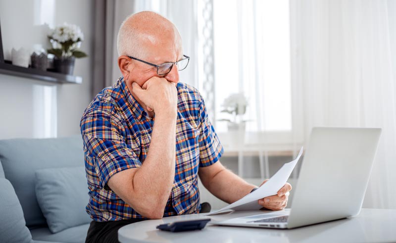 Privatmedizin in Österreich: Das stille Sterben des öffentlichen Kassensystems 2 Älterer Mann sitzt nachdenklich vor Laptop und Taschenrechner mit einer Arztrechnung in der Hand, Stichwort Privatmedizin in Österreich.(c) AdobeStock