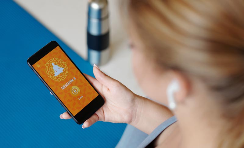 Analoge Zufluchtsorte: Warum das Reparieren alter Motoren oder Holzarbeit mehr Mentalthygiene ist als jede Meditation-App 1 Frau hält ein Smartphone mit geöffneter Meditations-App in der Hand.(c) AdobeStock