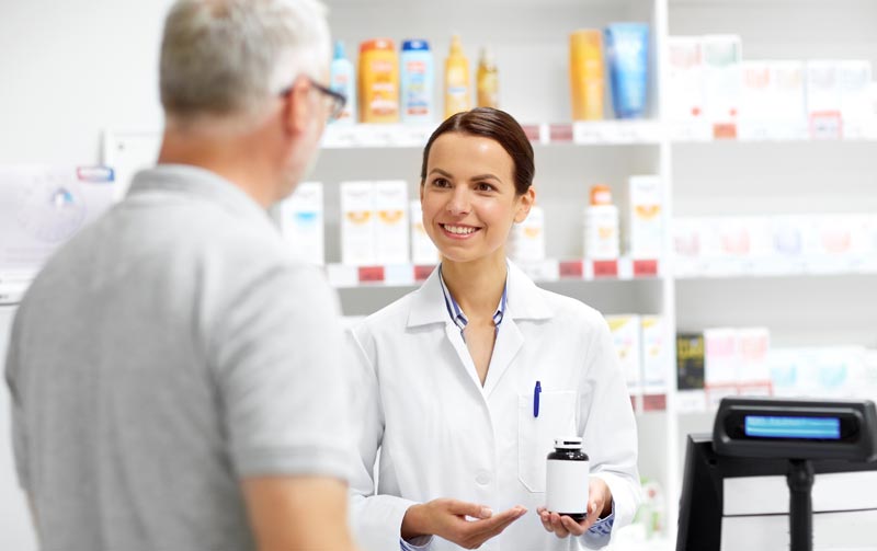 Wechselwirkungen von Medikamenten und Lebensmitteln: Die unsichtbare Gefahr am Teller 2 Apothekerin berät einen Kunden in einer modernen Apotheke und hält eine Medikamentenpackung in der Hand, Stichwort Wechselwirkungen Medikamente Lebensmittel.(c) AdobeStockk